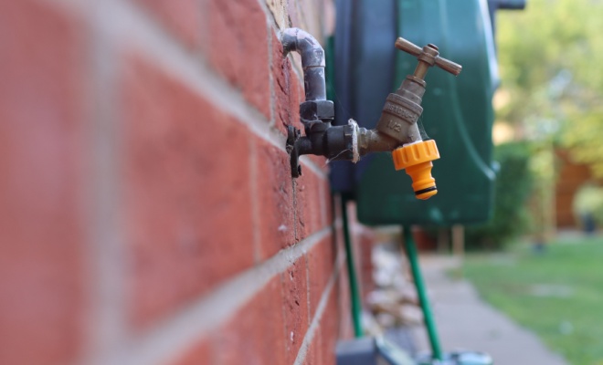tap on brick wall with blurred garden