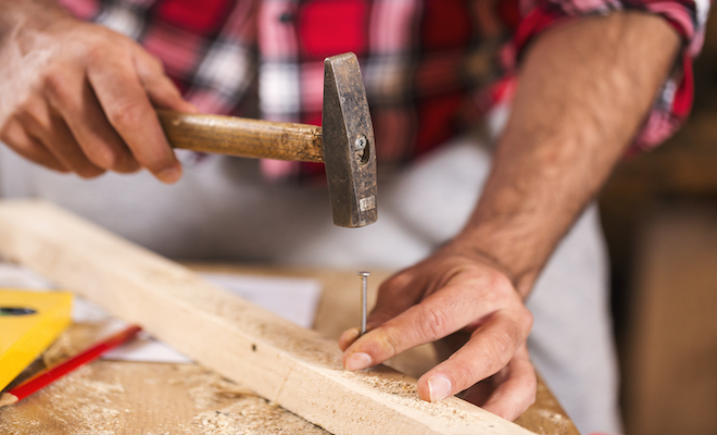 person hammering a nail in to wood