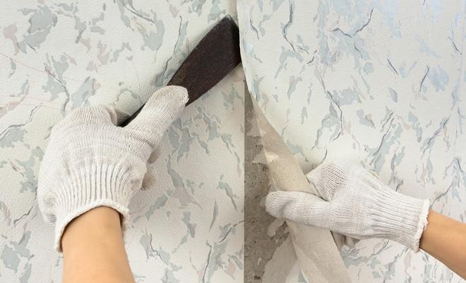 gloved hands stripping wallpaper with tool